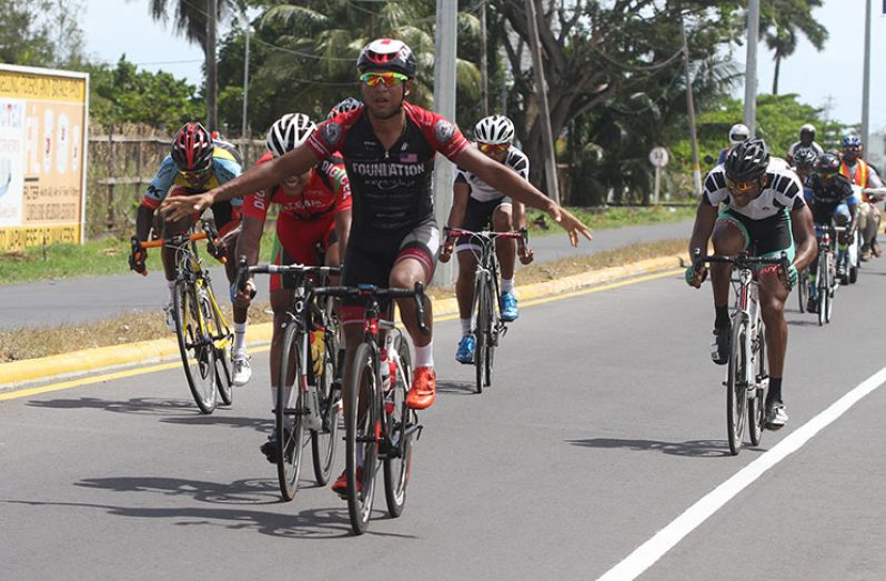 Geron Williams raises his arms in jubilation as he crosses the finish line in winning stage one of the NSC’s three-stage cycle road race yesterday ahead of Alonzo Greaves (partly hidden on Williams’ right).