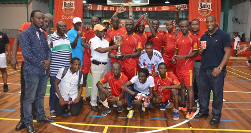 Winning Captain Phillip Rowley collecting the winners' trophy  from Minister of Foreign Affairs and first Vice-president Carl Greenidge surrounded by team mates and officials  of Champions Banks DIH.